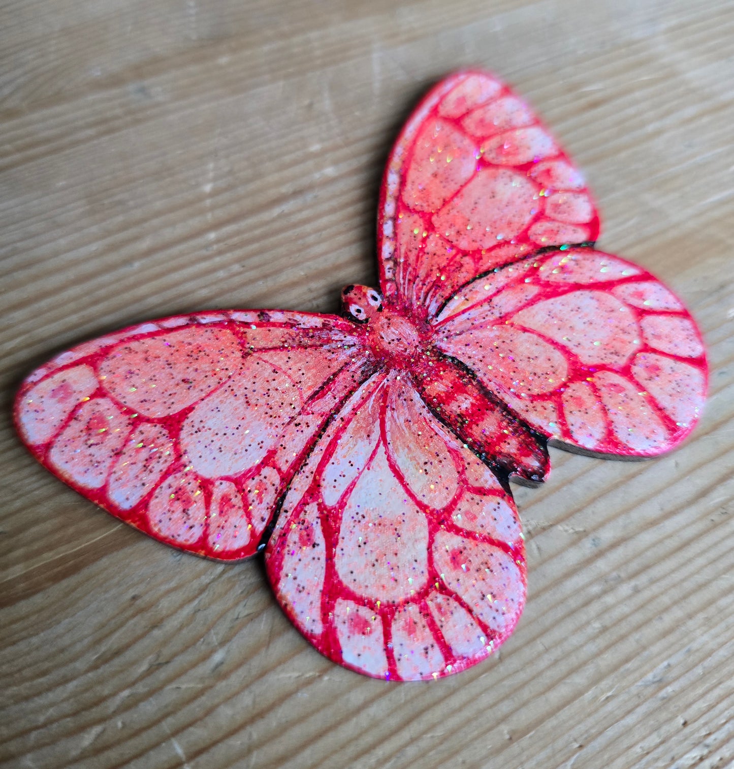 Liten håndmalt sommerfugl i rødt og fersken toner. med glitter i fernissen. Malt på lettet med magnetisk bakside. Brukt akrylmaling.Kjøleskapsmagnet.