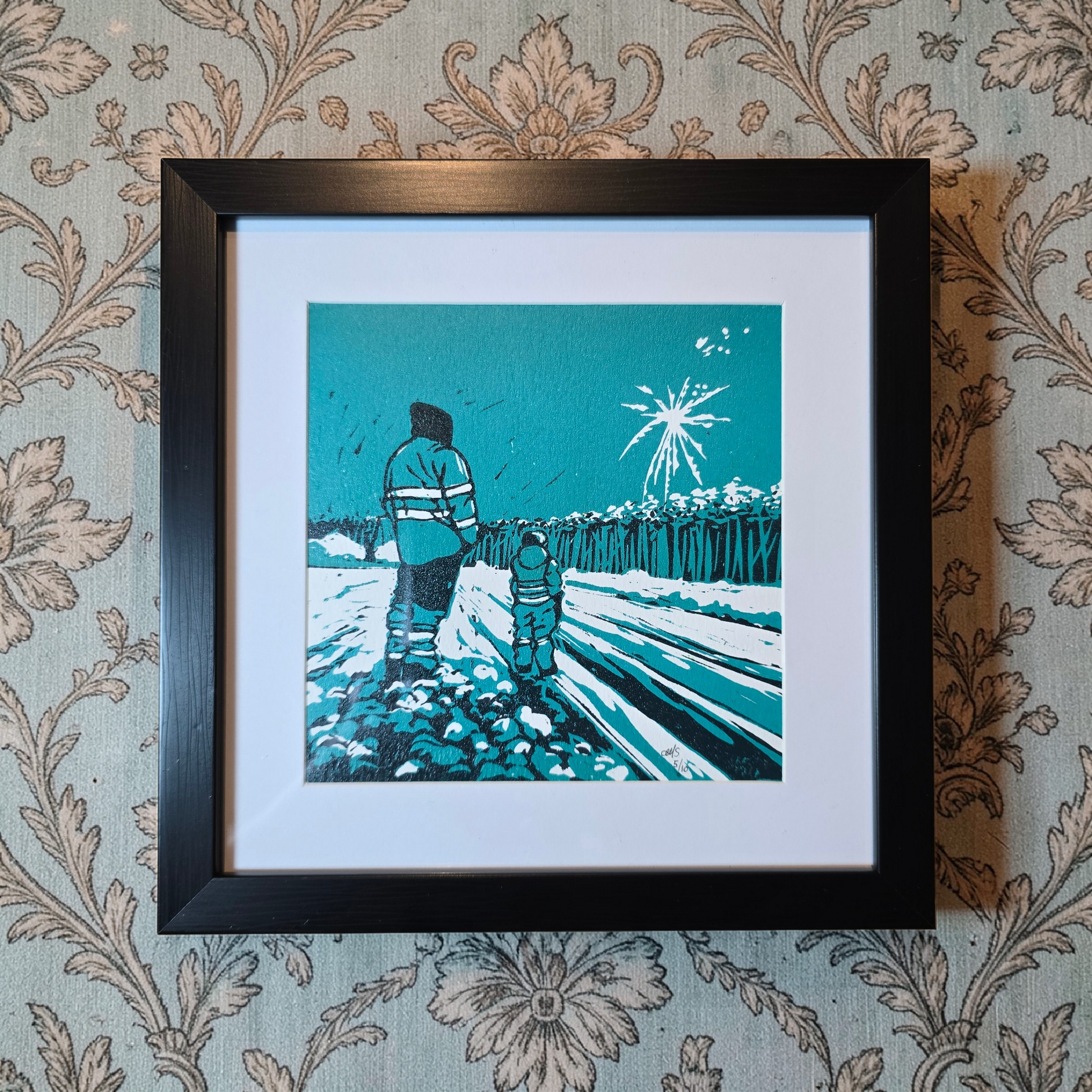 Linotrykk Far og sønn. Dette er nummerert  5 av 10.Trykket viser en far og sønn som står og ser nyttårsfyrverkeri sammen. En koselig stund. Trykket er trykket i blågrønt, mørk og lyst. så er det også hvitt fra arket. Hvit passeopartout og svart ramme i kunststoff.