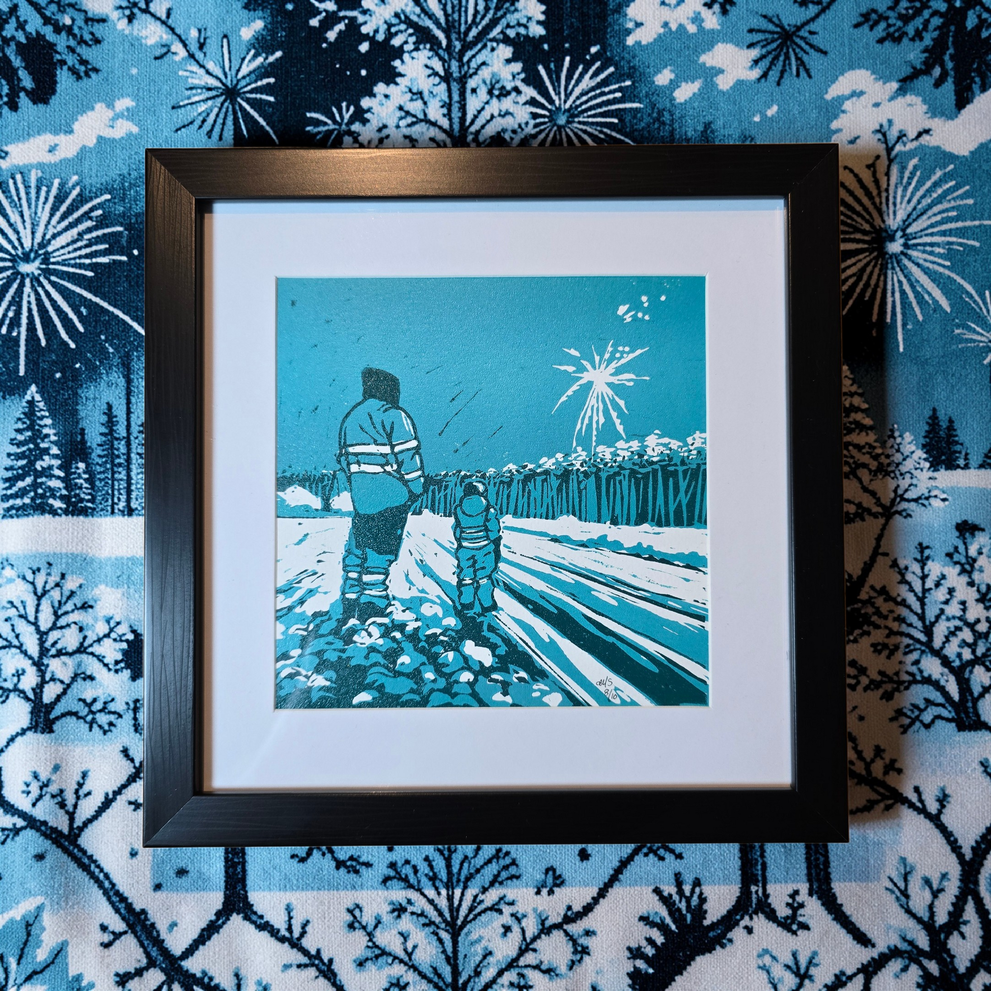 Linotrykk Far og sønn. Dette er nummerert  8 av 10.Trykket viser en far og sønn som står og ser nyttårsfyrverkeri sammen. En koselig stund. Trykket er trykket i blågrønt, mørk og lyst. så er det også hvitt fra arket. Hvit passeopartout og svart ramme i kunststoff.