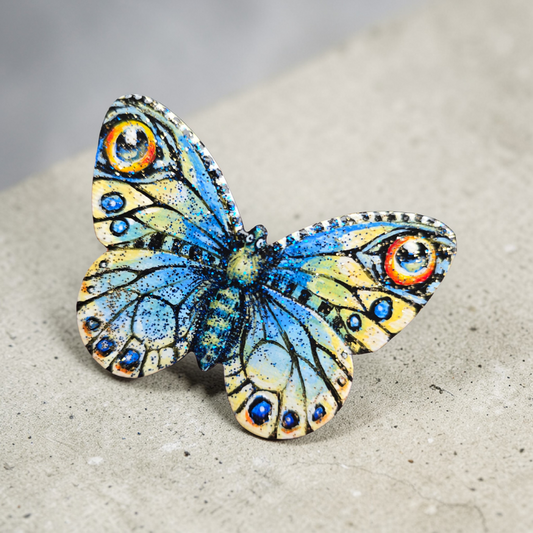 Sommerfugl i blått og gult med øyetegninger. Blått og gull glitter i den blanke fernissen Liten kjøleskapsmagnet håndmalt på sommerfuglfasonglerret.